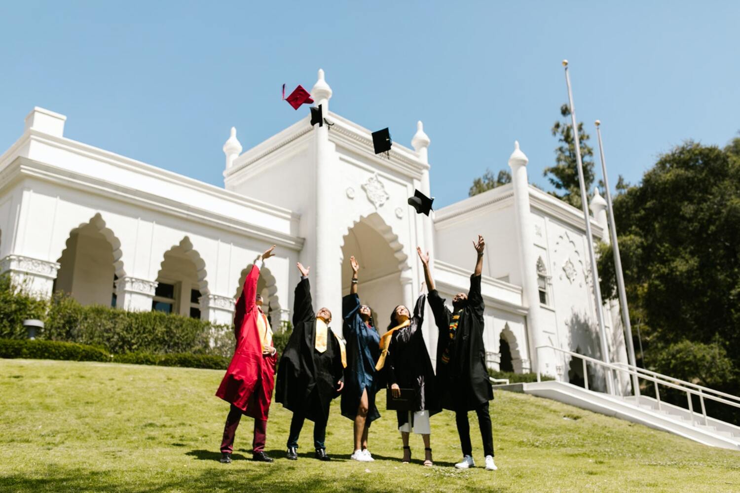 College students in caps and gowns standing outside a college celebrating by throwing caps in the air