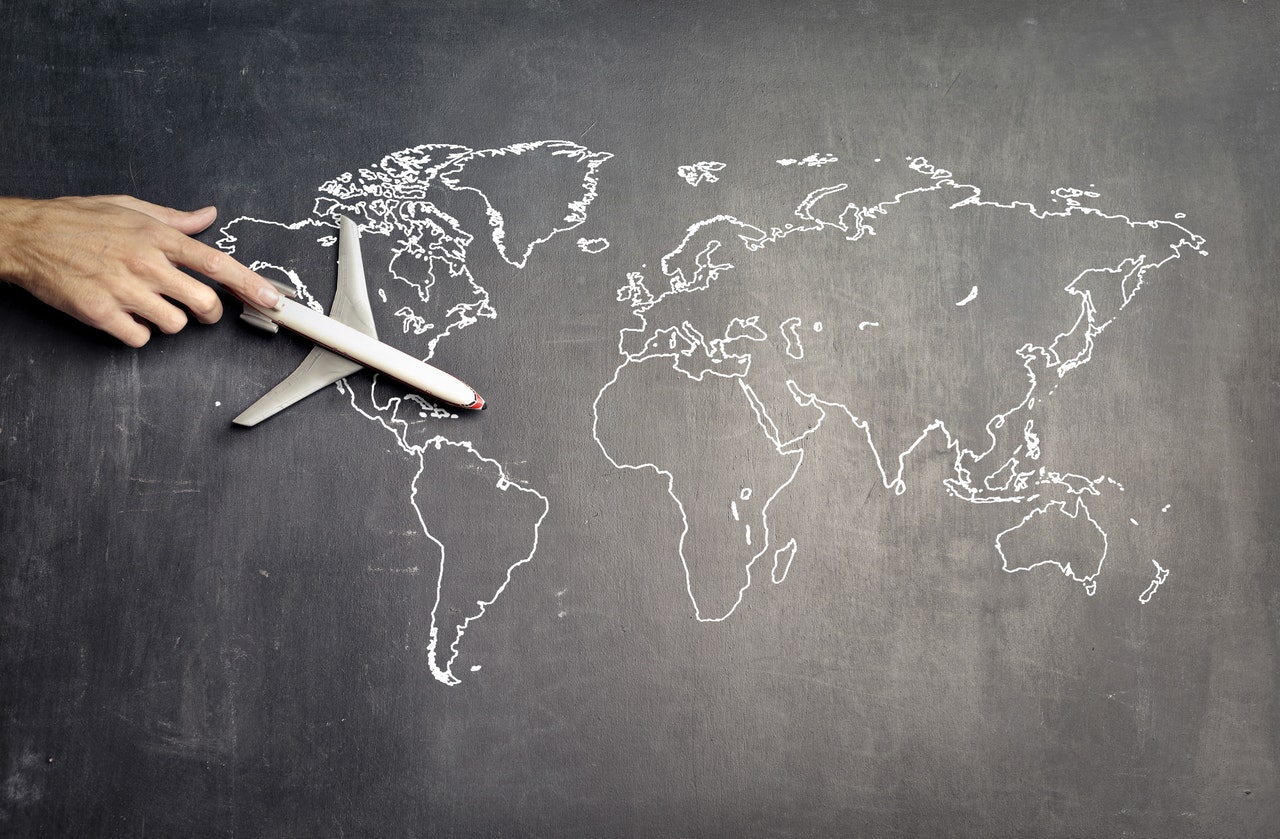 Map of the world on a chalkboard with a hand holding an airplane model