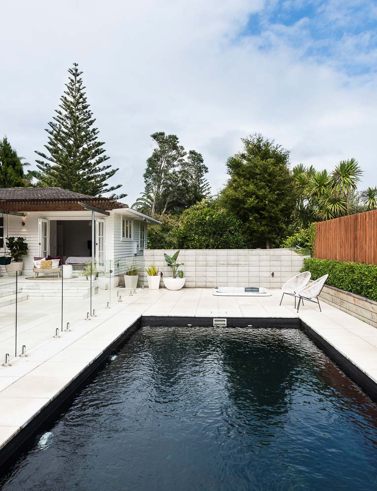 Black tile pool with white concrete and chairs.