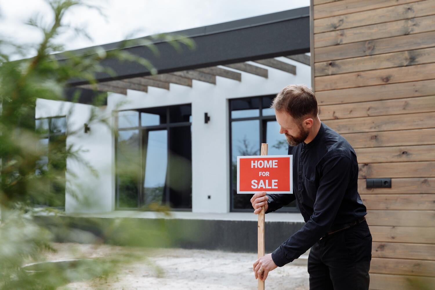 A man with a house for sale sign infront of a home.