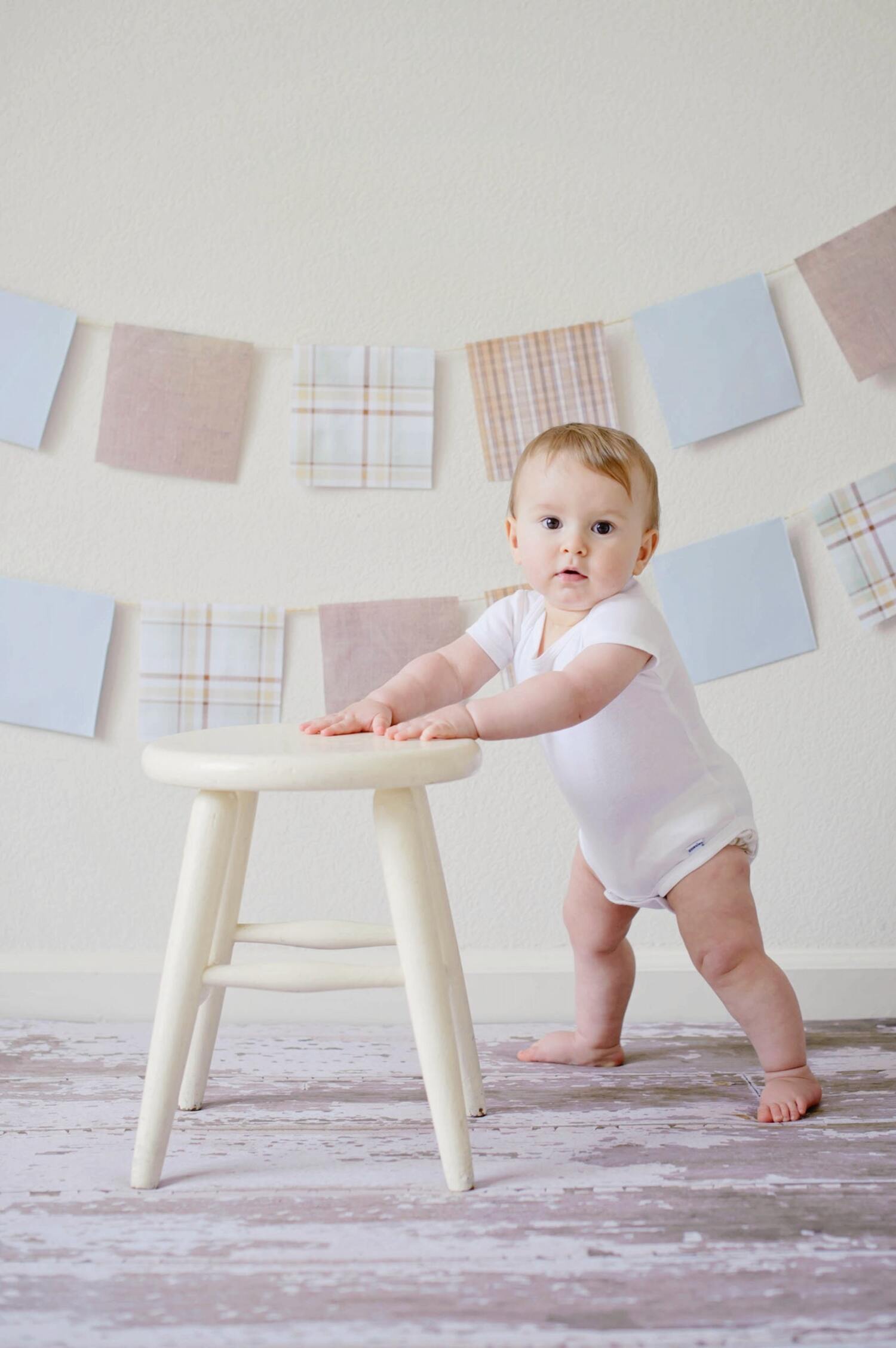 A baby growing and standing near a stool.