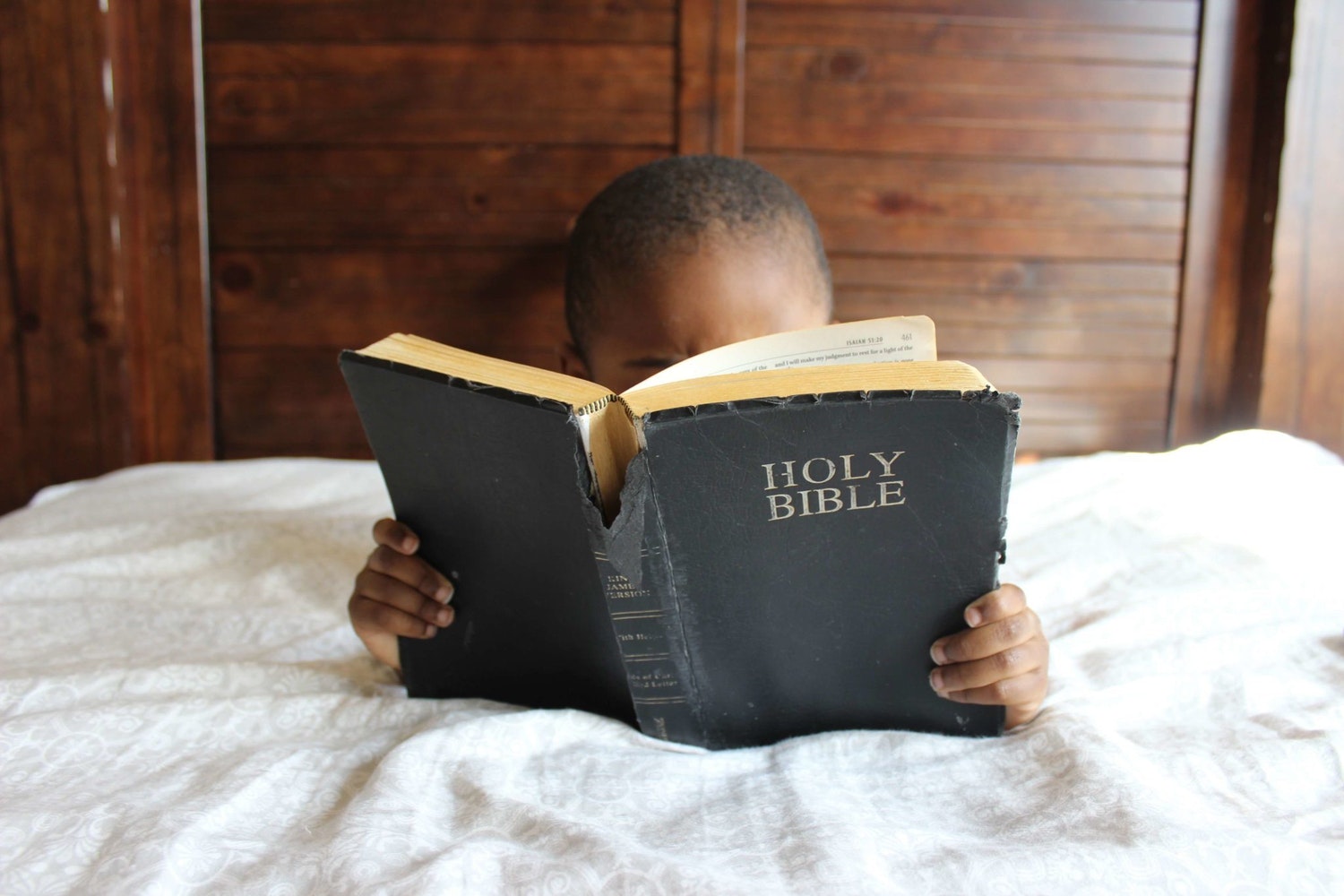 A child in bed reading Bible verses.