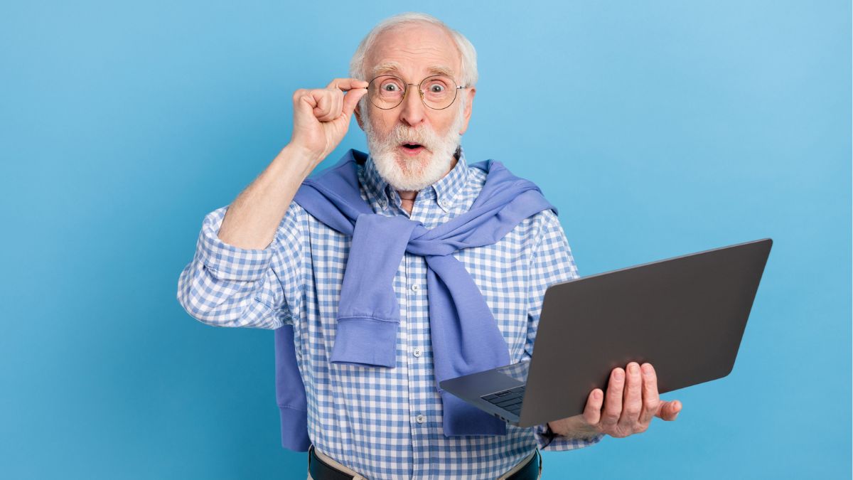 elder man wearing a sweater and holding laptop