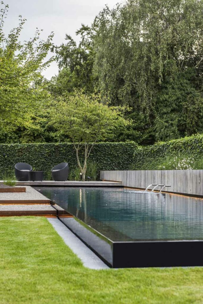 Large dark tile pool in green backyard.