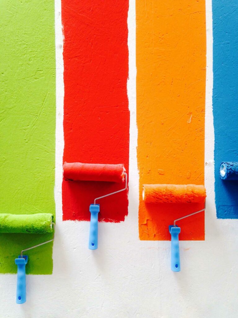 Paint rollers with different colors of paint on a wall.