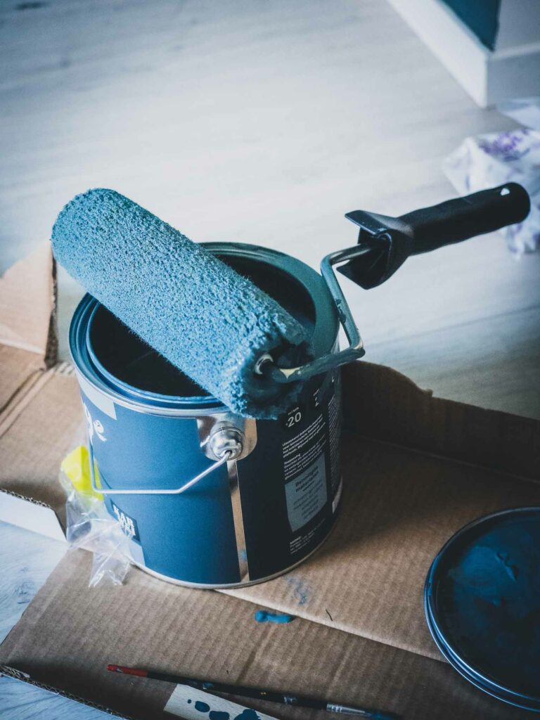 Paint roller with blue paint bucket.