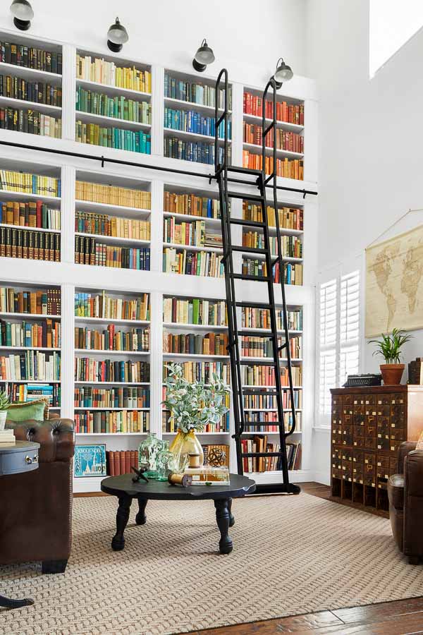 Two story wall with colorful bookshelves and tall ladder.