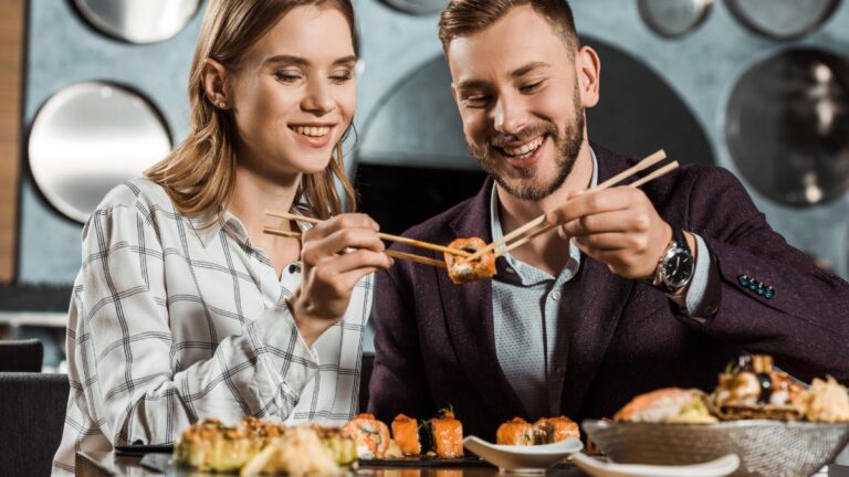 Smiling attractive young adult couple eating sushi together in restaurant