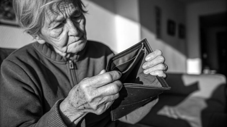 An elderly person with weathered hands holding a nearly empty wallet