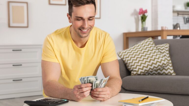 Happy man counting money at table in living room