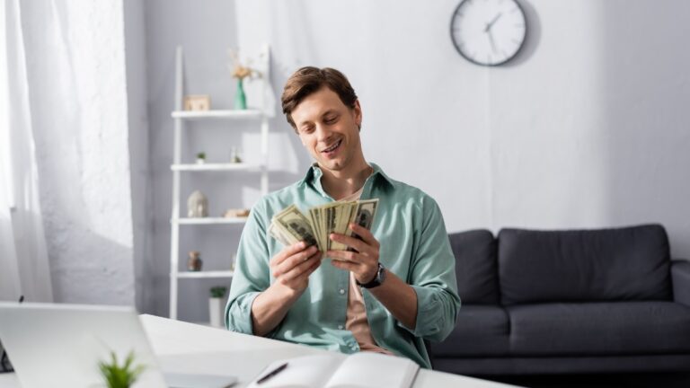 Selective focus of smiling man counting money near laptop