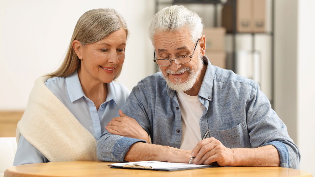 Smiling senior couple signing Last Will and Testament indoors