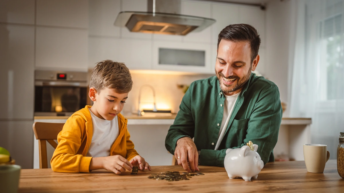 Father and son save money coins together at piggy bank at home