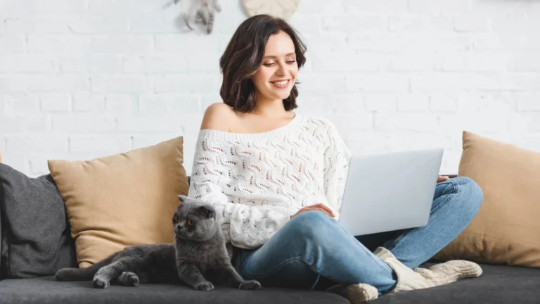 Smiling girl using laptop with scottish fold cat on sofa