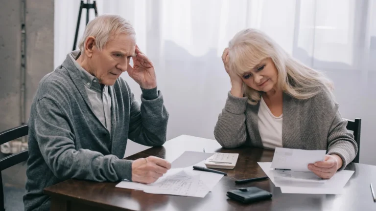 Stressed senior couple with hands on head sitting at table