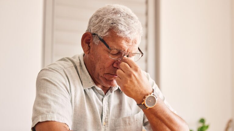 headache and old man at table in home with glasses