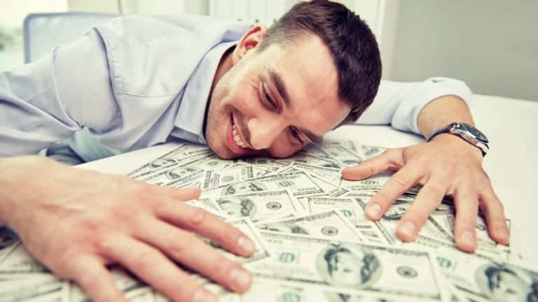 Happy businessman with heap of money in office