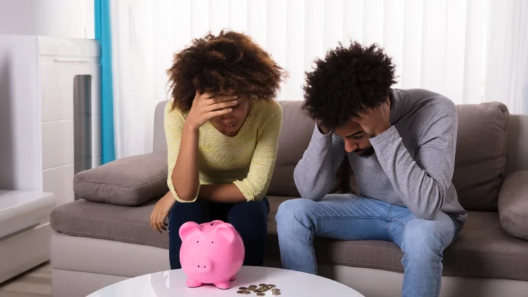 Sad Couple Sitting On Sofa With Piggybank And Coins