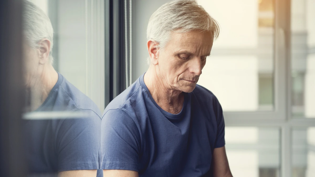 Sad mature man sitting on windowsill