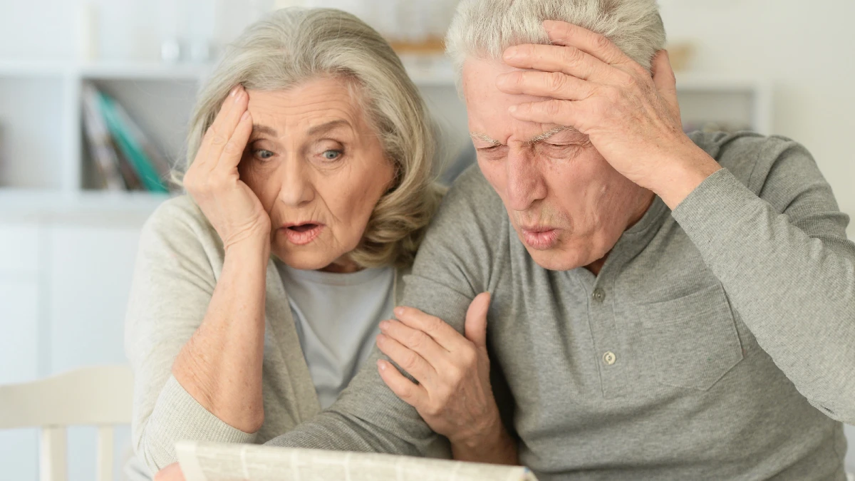 Close-up portrait of a senior couple with newspaper at home