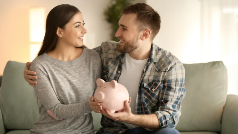 Happy couple sitting on sofa and holding piggy bank indoors.