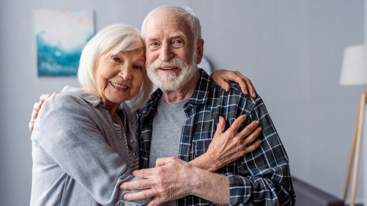 Happy senior couple smiling and embracing while looking at camera