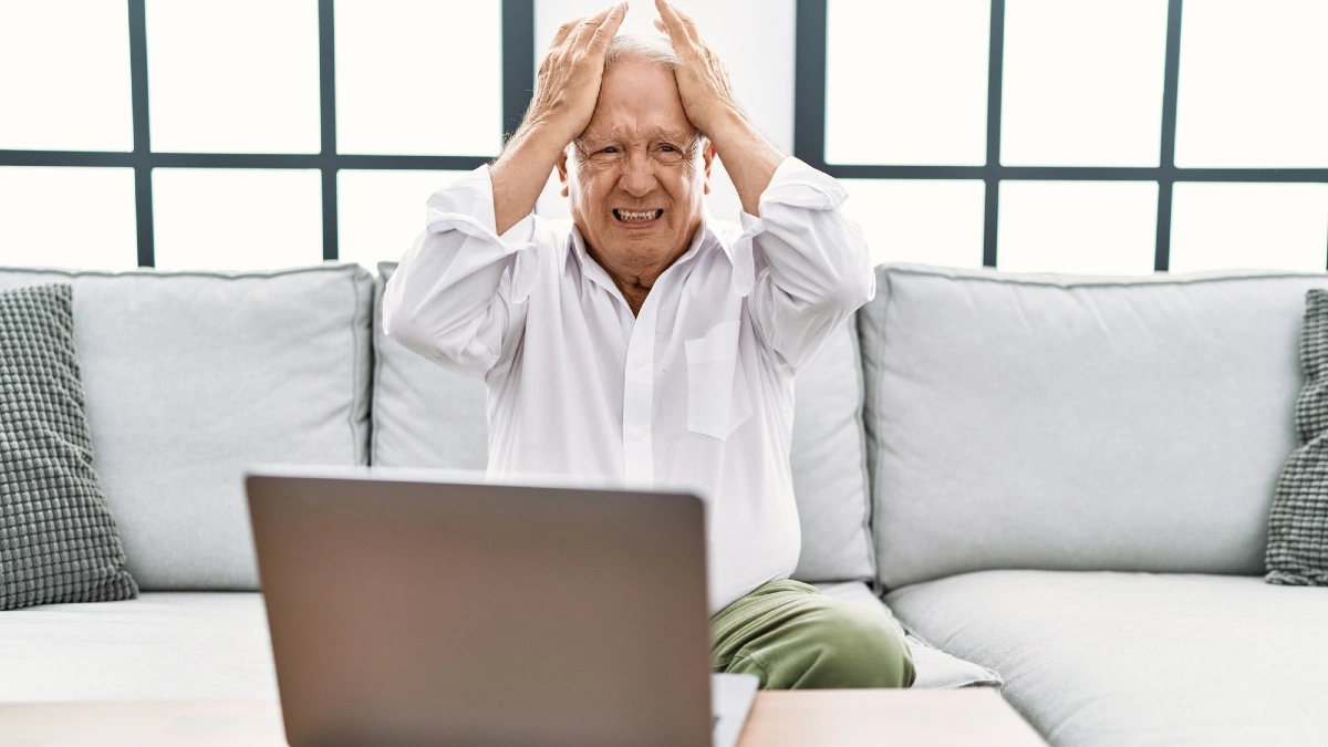 Senior man using laptop at home sitting on the sofa suffering