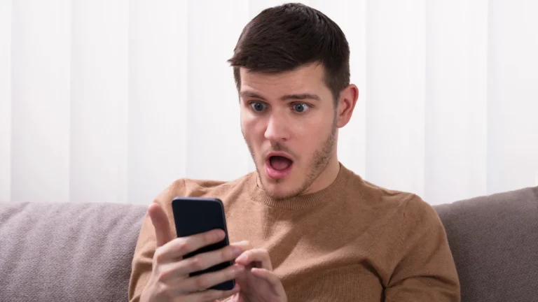 Shocked Young Man Sitting On Sofa And Looking